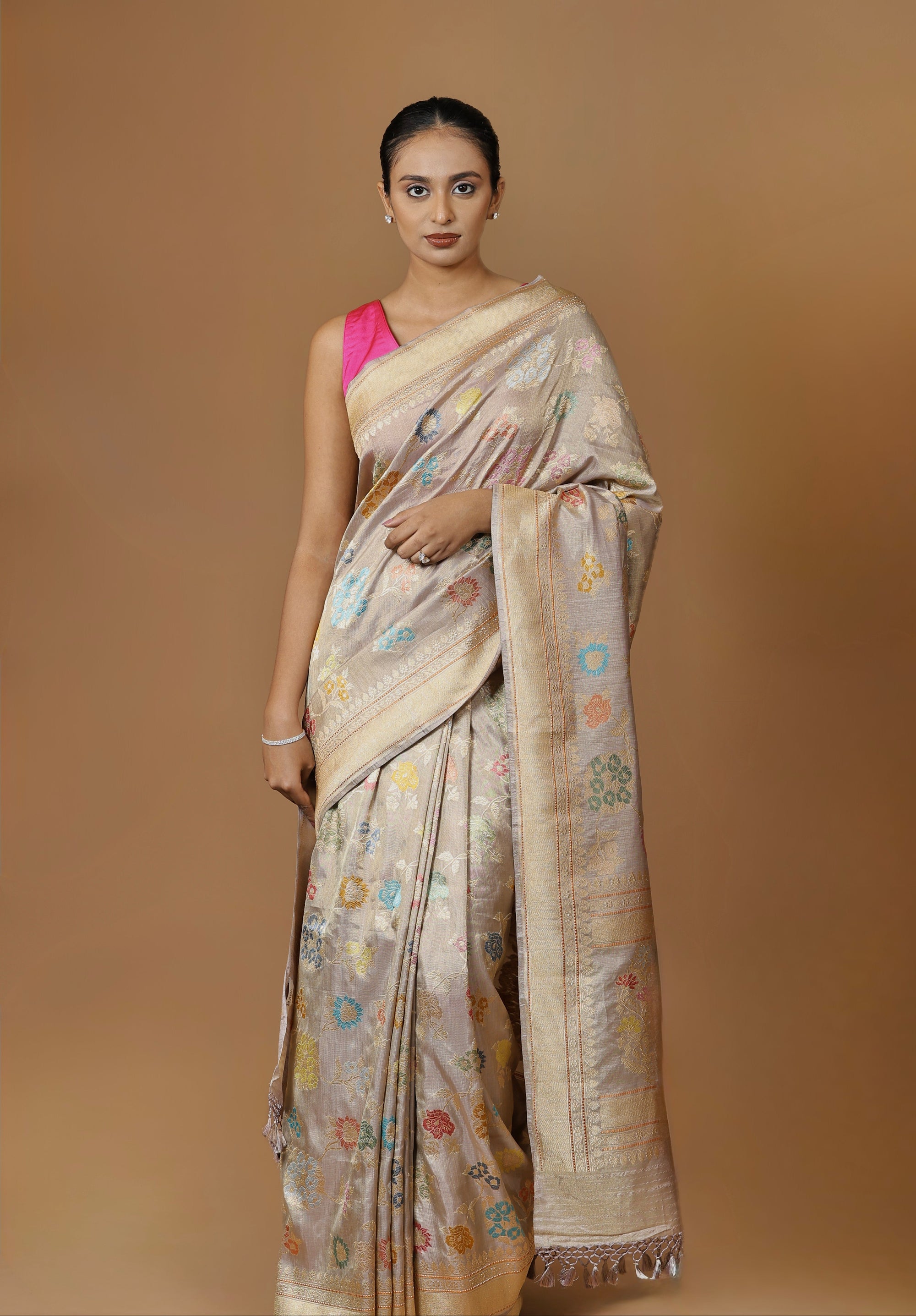Handwoven Banarasi tissue silk sari in soft silver, featuring vibrant meenakari floral motifs and a golden border.