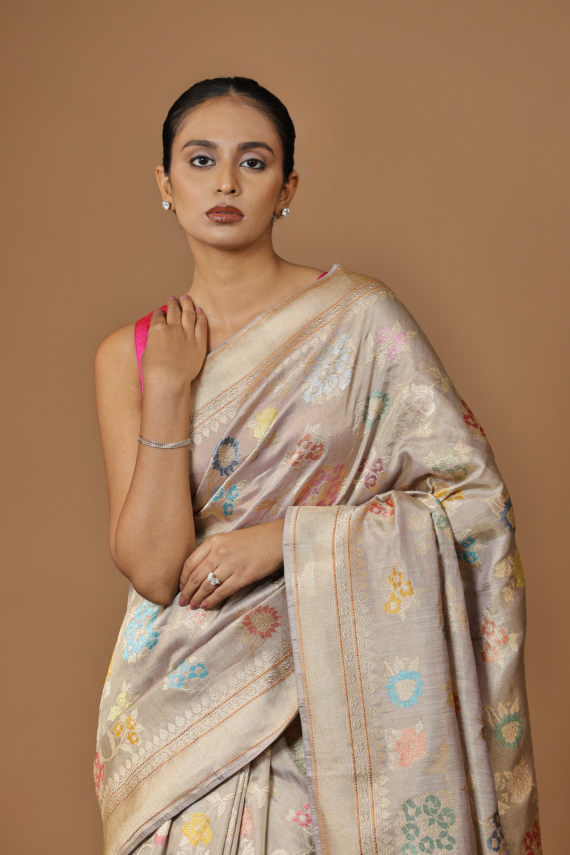 Handwoven Banarasi tissue silk sari in soft silver, featuring vibrant meenakari floral motifs and a golden border.